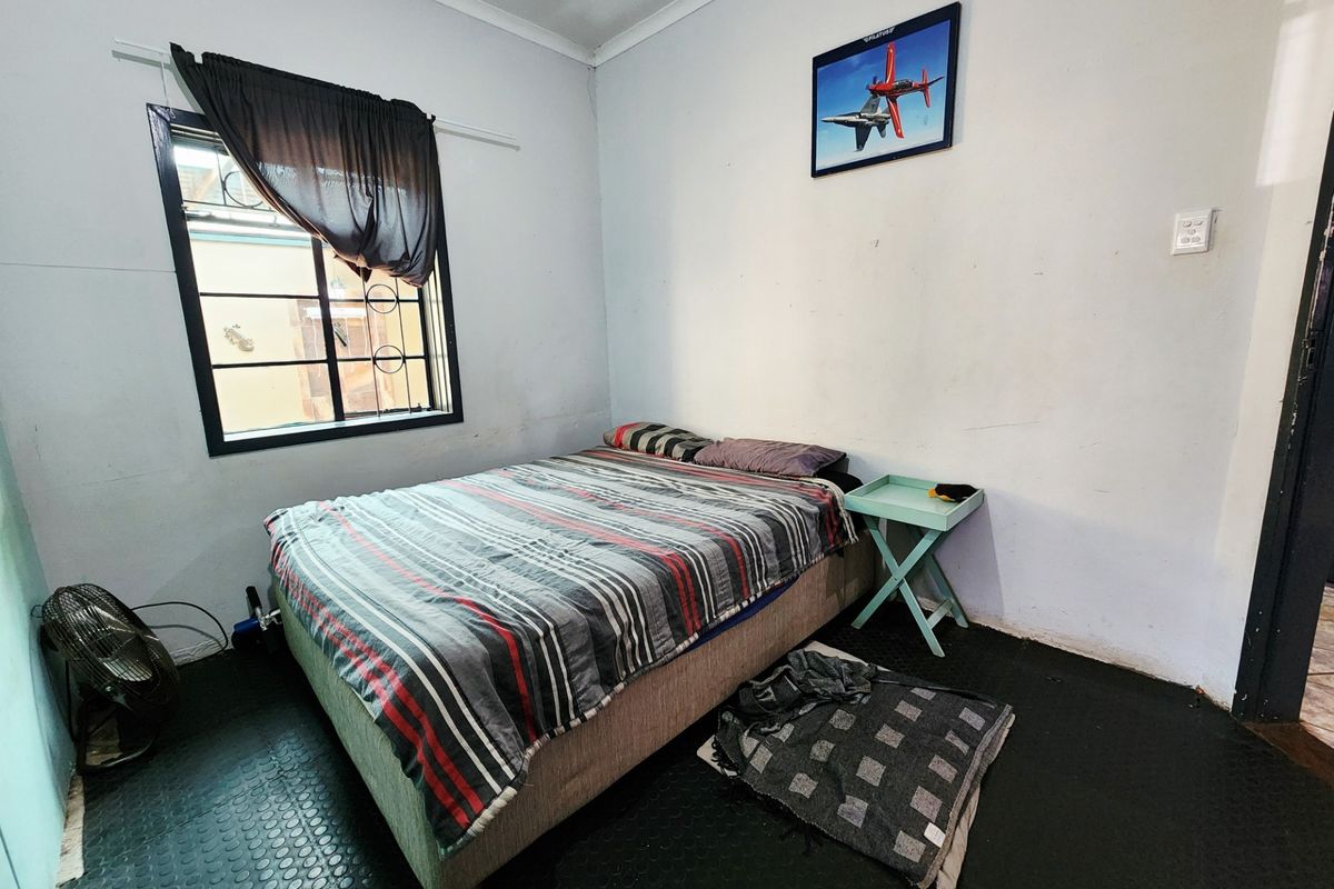 A bedroom featuring a window with security bars and coving, currently requiring cosmetic updates to the wall finishes and flooring.