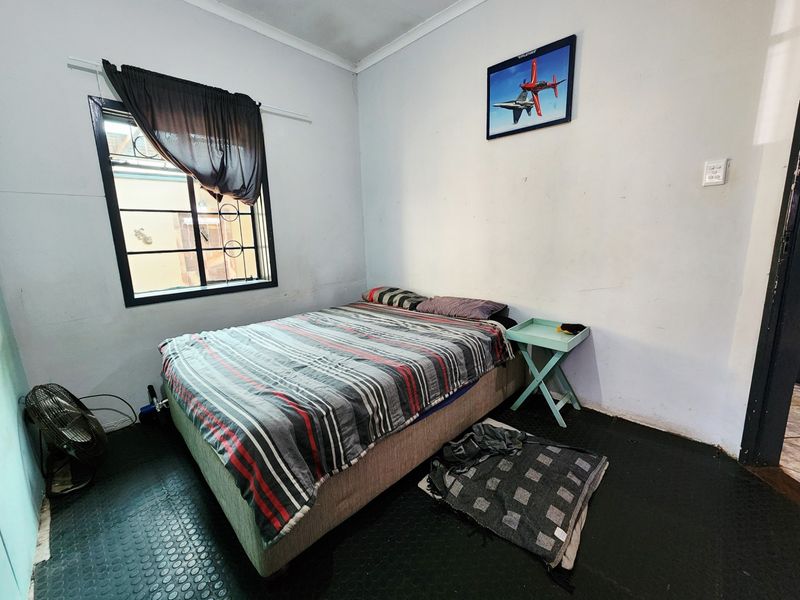 A bedroom featuring a window with security bars and coving, currently requiring cosmetic updates to the wall finishes and flooring.