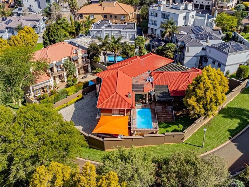 Aerial view of a residential property featuring a tiled roof, private swimming pool, wooden deck, and paved driveway within a secure estate setting.