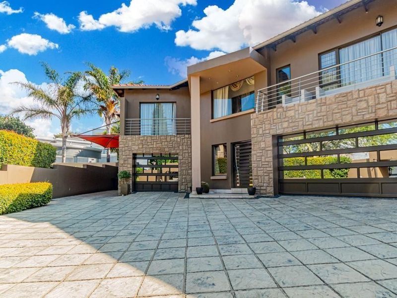 Modern double-story residence featuring stone cladding, a spacious paved driveway, and integrated double garage with balcony access.