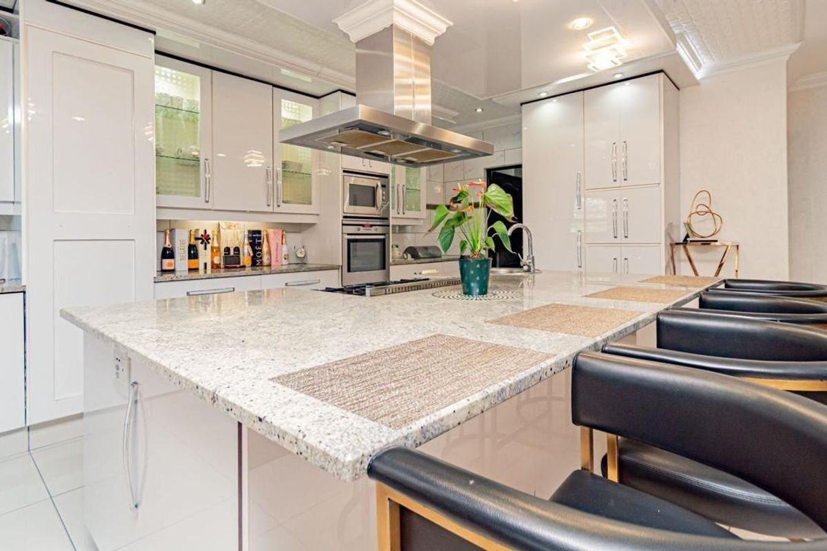 Modern kitchen featuring high-gloss cabinetry, granite countertops, a large central island with breakfast bar seating, and integrated stainless steel appliances.