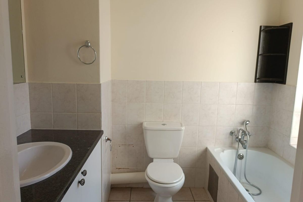 A functional bathroom featuring a vanity with integrated sink, a standard toilet, and a bathtub with shower mixer, finished with neutral wall and floor tiles.