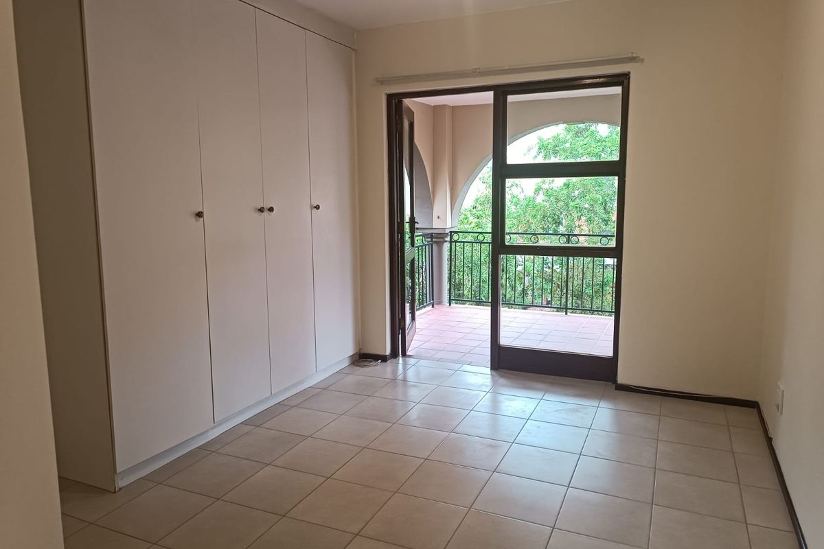 A bright, empty bedroom featuring built-in cupboards, tiled flooring, and direct access to a private balcony through a sliding glass door.