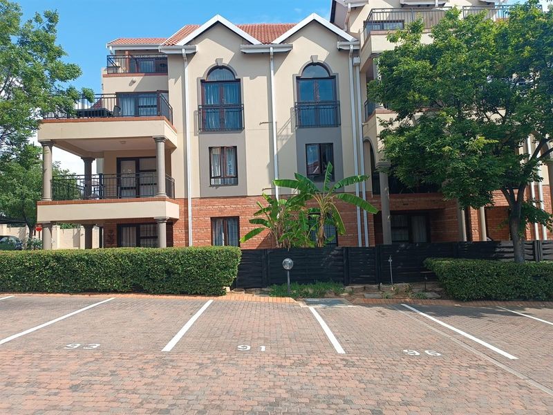 Exterior view of a multi-story apartment complex featuring brick and plaster facade, arched windows, private balconies, and designated paved parking bays.
