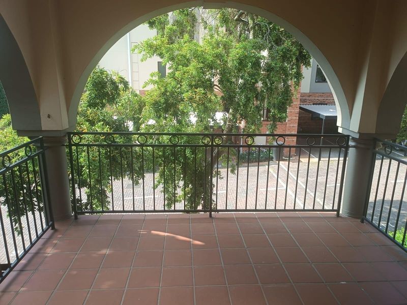 A covered balcony featuring tiled flooring, a decorative wrought iron balustrade, and an arched architectural opening overlooking the complex grounds.