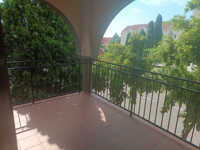 A covered balcony featuring tiled flooring and a decorative wrought iron balustrade, offering an elevated view of the surrounding greenery and street.