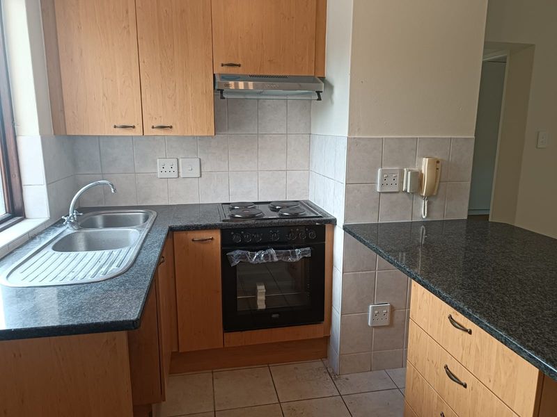 A functional kitchen featuring laminate cabinetry, granite countertops, a built-in oven with hob, and an extractor fan, finished with ceramic wall and floor tiles.