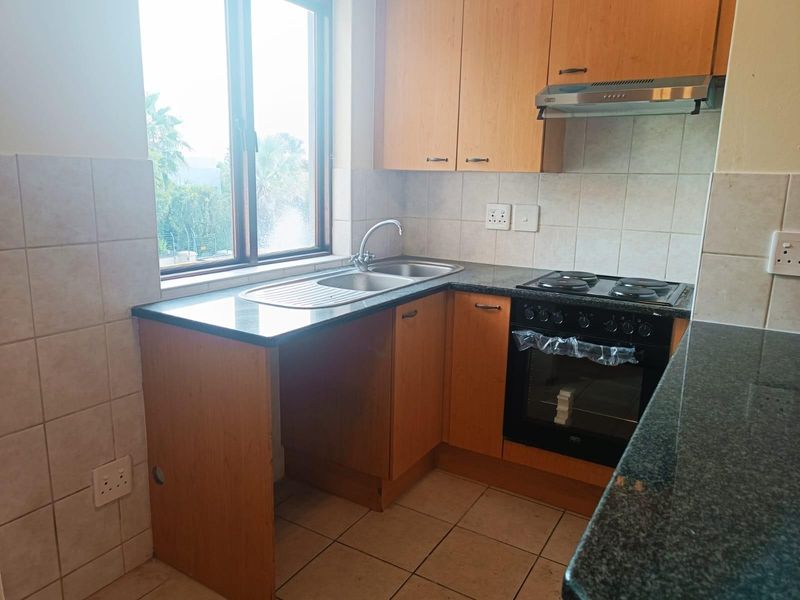Functional kitchen featuring laminate cabinetry, granite countertops, built-in oven, electric hob, extractor fan, and tiled splashback with natural light.