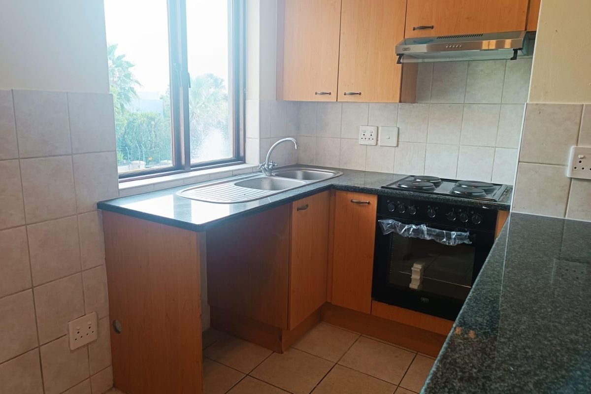 Functional kitchen featuring laminate cabinetry, granite countertops, built-in oven, electric hob, extractor fan, and tiled splashback with natural light.