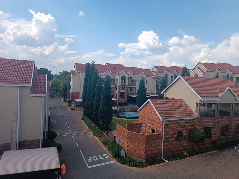An elevated view of a residential apartment complex featuring multiple buildings with tiled roofs, paved driveways, and a communal swimming pool area.
