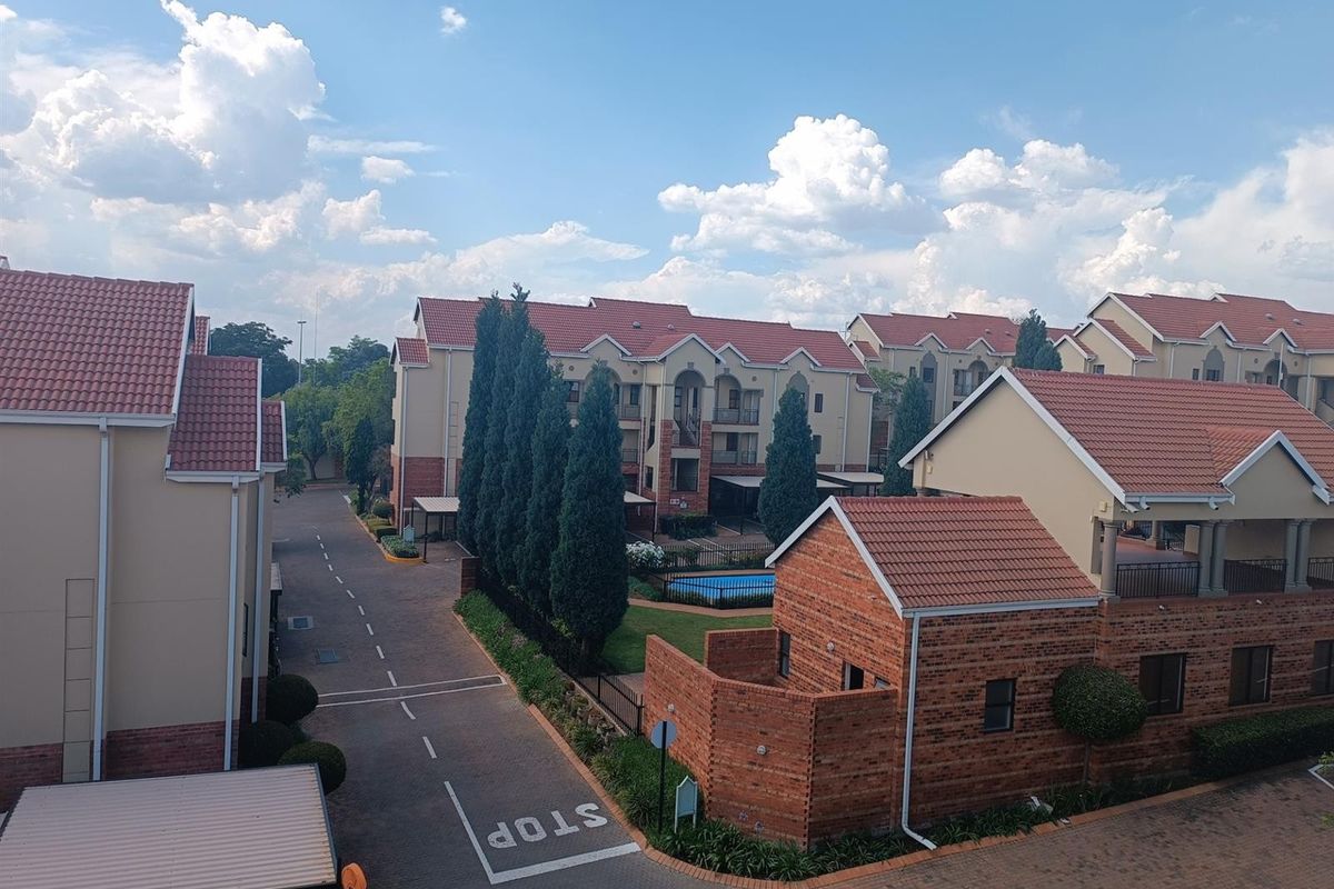 An elevated view of a residential apartment complex featuring multiple buildings with tiled roofs, paved driveways, and a communal swimming pool area.