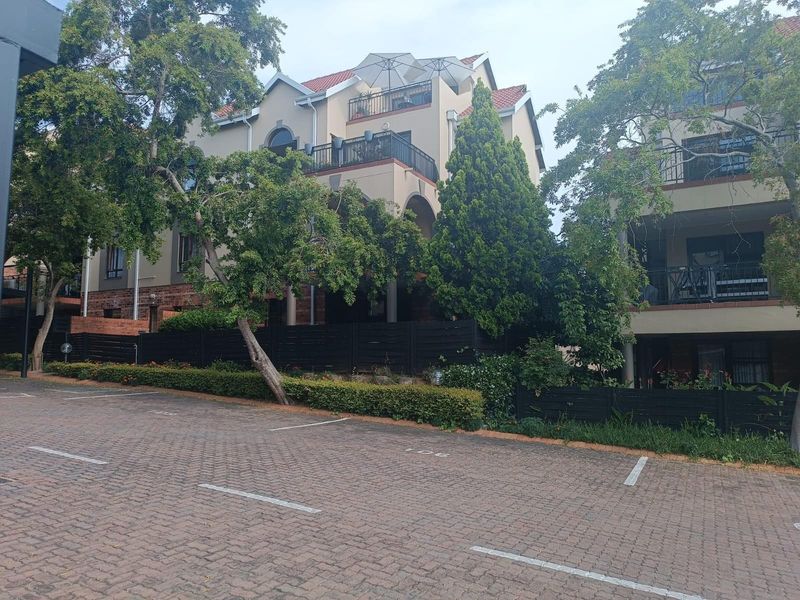 Exterior view of a multi-story apartment complex featuring paved parking, balconies, and established landscaping.