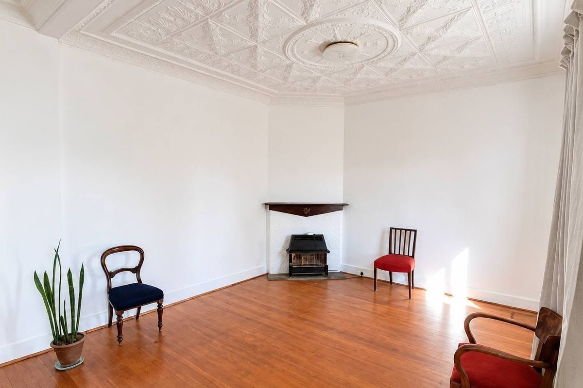 Spacious living room featuring original ornate pressed metal ceilings, polished timber flooring, and a classic corner fireplace with a timber mantelpiece.