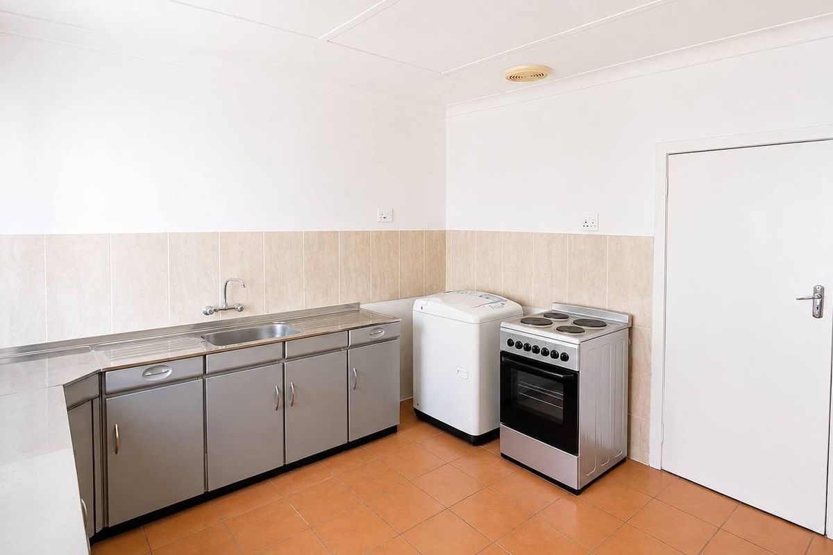 A functional kitchen featuring tiled flooring, neutral splashback tiles, stainless steel cabinetry, and a freestanding electric stove.