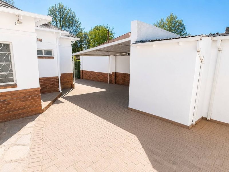 A clean, paved rear courtyard area featuring a covered carport and well-maintained brick and white-painted exterior walls.