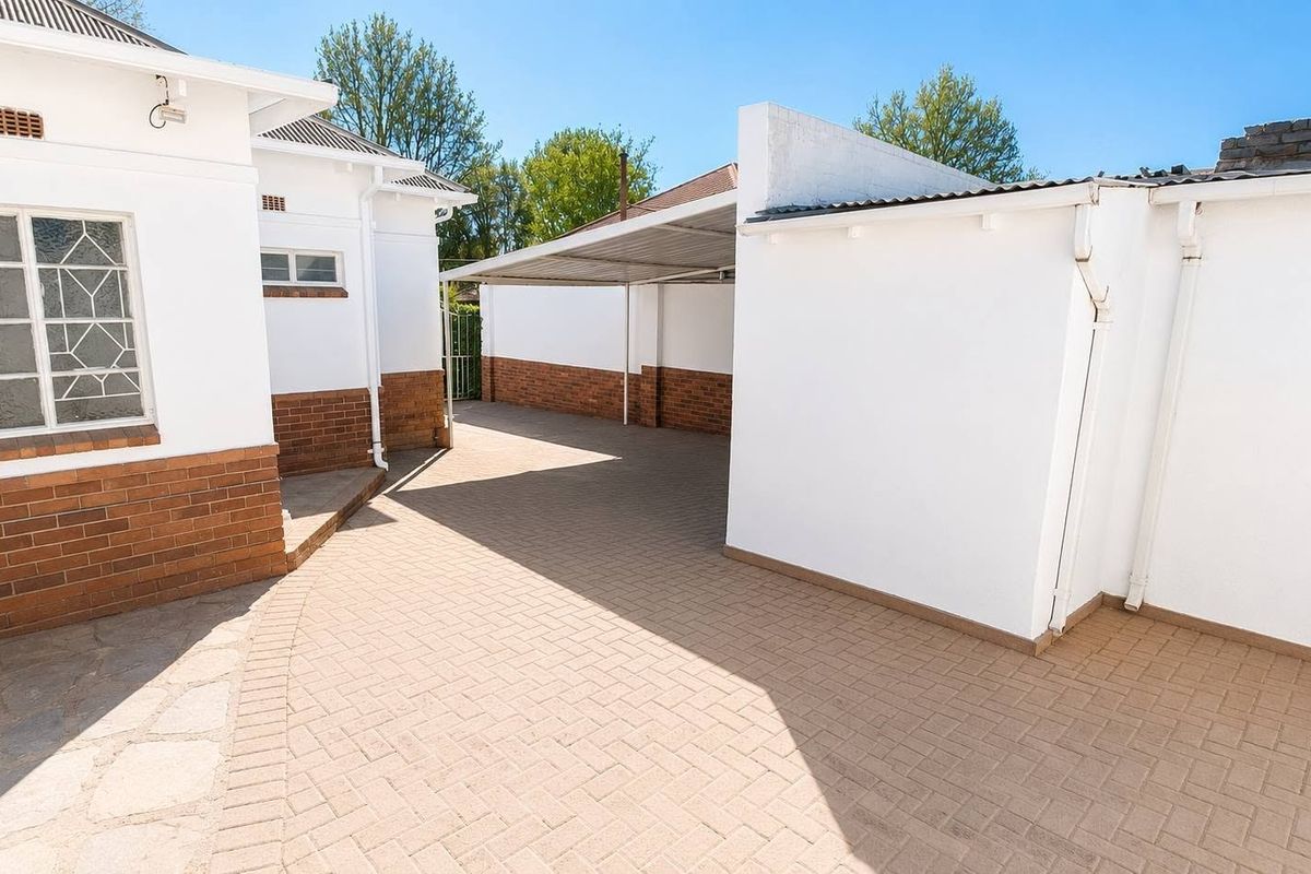 A clean, paved rear courtyard area featuring a covered carport and well-maintained brick and white-painted exterior walls.