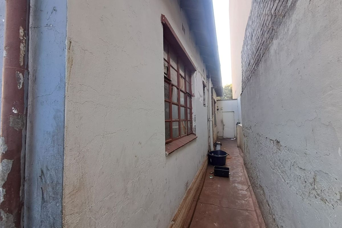 A narrow side passage of the property featuring weathered exterior walls, a steel-framed window, and a concrete pathway requiring maintenance.