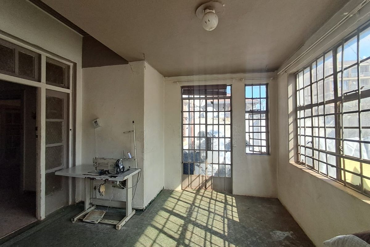 A sunlit, vacant living area featuring metal-framed windows, a security gate, and original flooring, offering a blank canvas for renovation and modernization.