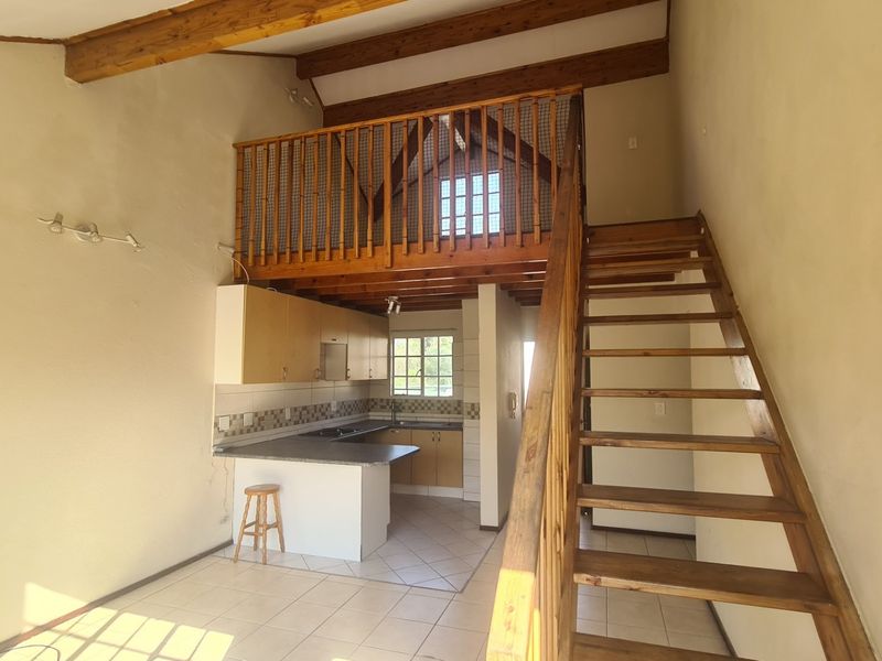 Open plan living area featuring a kitchen with built-in cabinetry, tiled flooring, and a timber staircase leading to a mezzanine level with exposed beams.
