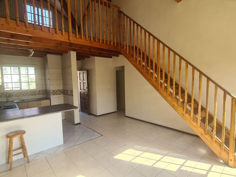 Open plan living area featuring a wooden staircase leading to a mezzanine level, tiled flooring, and a functional kitchen space.