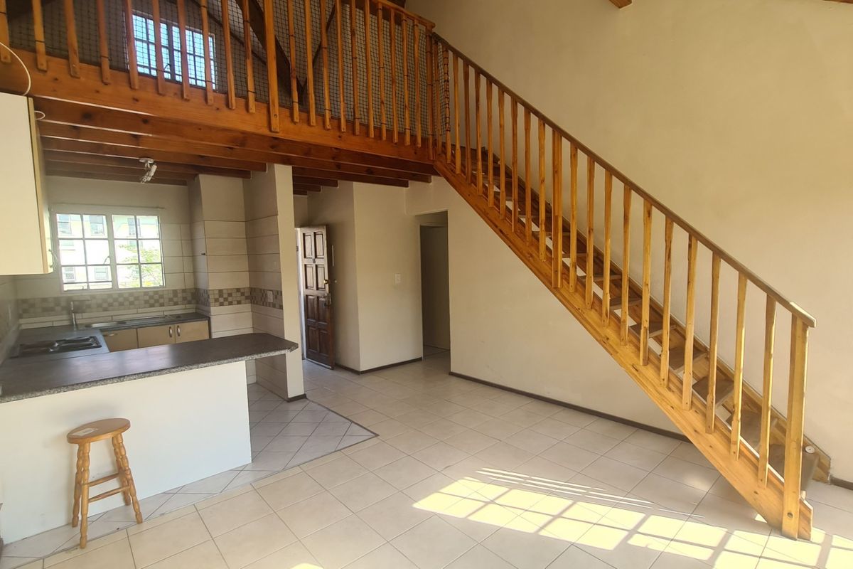Open plan living area featuring a wooden staircase leading to a mezzanine level, tiled flooring, and a functional kitchen space.