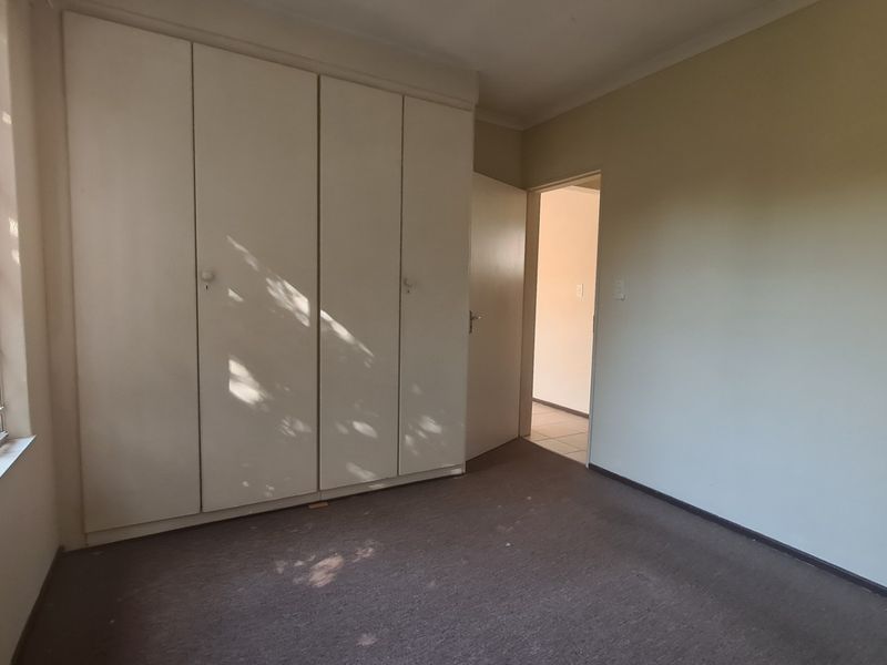 A vacant bedroom featuring built-in cupboards, large windows for natural light, and carpeted flooring, offering a blank canvas for personalization.