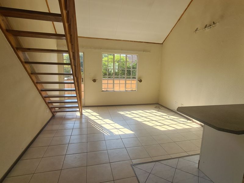 An open-plan living area featuring tiled floors, a vaulted ceiling, and a wooden staircase leading to an upper level.