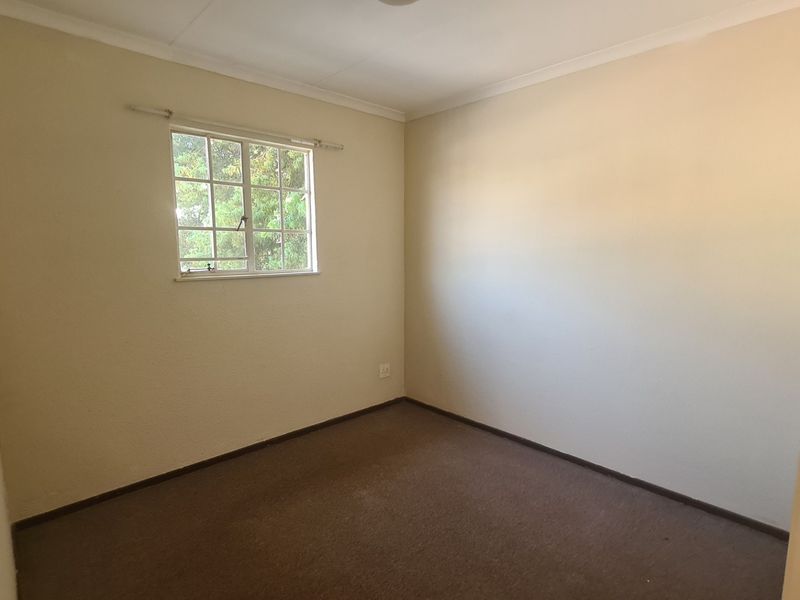 A clean, empty bedroom featuring neutral walls, carpeted flooring, and a built-in cupboard, offering a blank canvas for personalization.