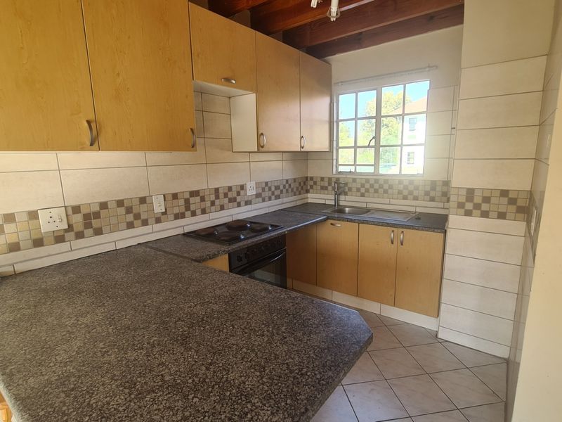 A functional kitchen featuring laminate cabinetry, granite-look countertops, built-in oven and hob, and exposed timber ceiling beams with tiled flooring.