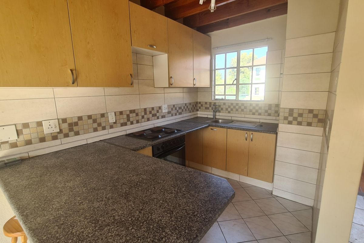 A functional kitchen featuring laminate cabinetry, granite-look countertops, built-in oven and hob, and exposed timber ceiling beams with tiled flooring.