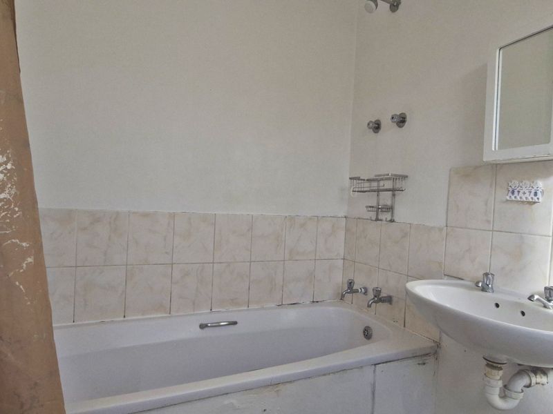 A dated bathroom featuring a standard bathtub, wall-mounted basin, and medicine cabinet, requiring cosmetic updates to improve its overall condition and appeal.