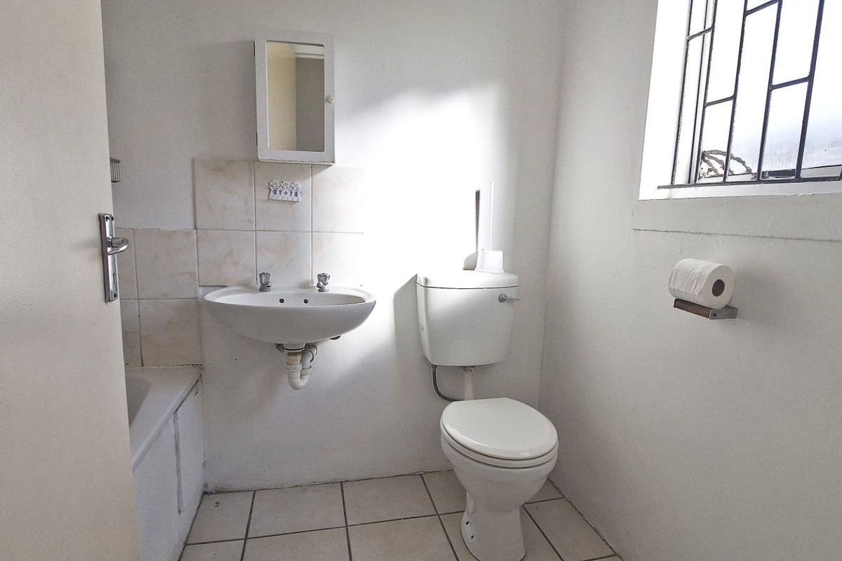 A functional bathroom featuring a pedestal basin, toilet, and bathtub with tiled flooring and a window with security bars.