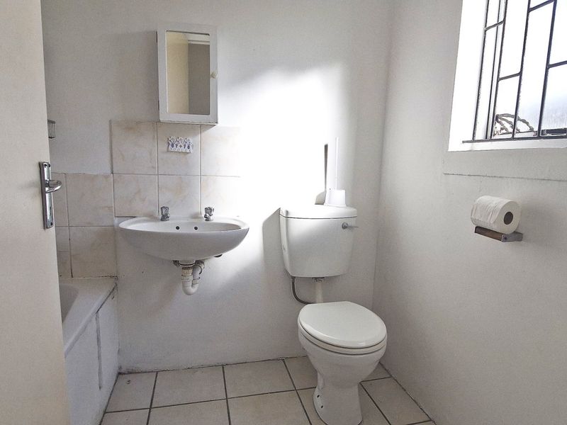 A functional bathroom featuring a pedestal basin, toilet, and bathtub with tiled flooring and a window with security bars.