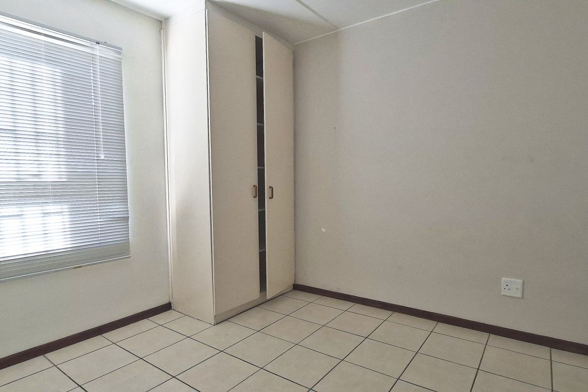 A clean, empty bedroom featuring neutral tiled flooring, a built-in wardrobe, and venetian blinds, offering a blank canvas for personalization.
