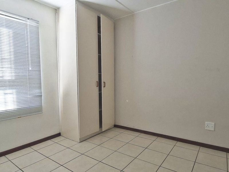 A clean, empty bedroom featuring neutral tiled flooring, a built-in wardrobe, and venetian blinds, offering a blank canvas for personalization.