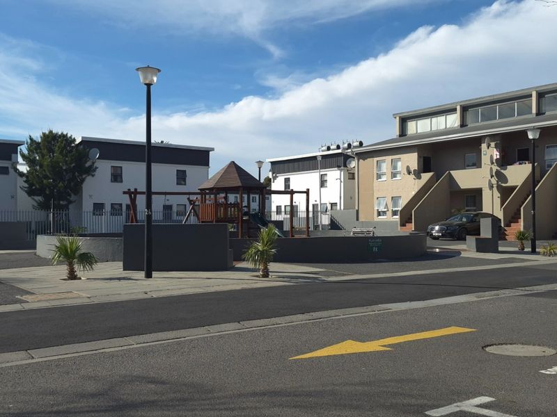 Exterior view of an apartment complex featuring a paved driveway, communal playground area, and multi-story residential buildings.