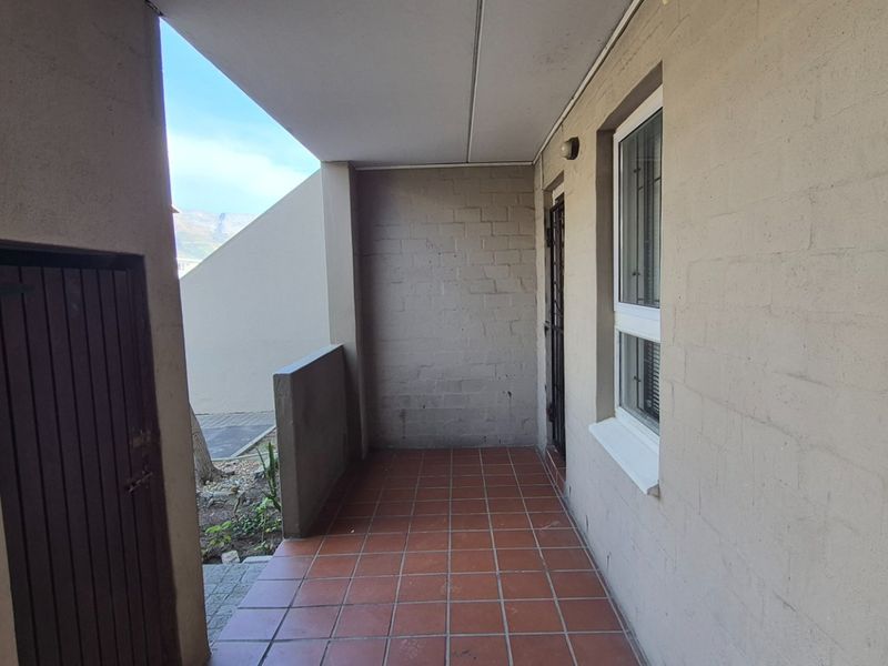 A covered outdoor patio area featuring tiled flooring, a security gate, and access to the apartment entrance.