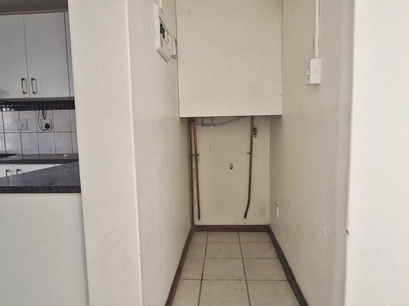 A dedicated laundry alcove featuring tiled flooring and exposed plumbing connections, adjacent to the kitchen area.