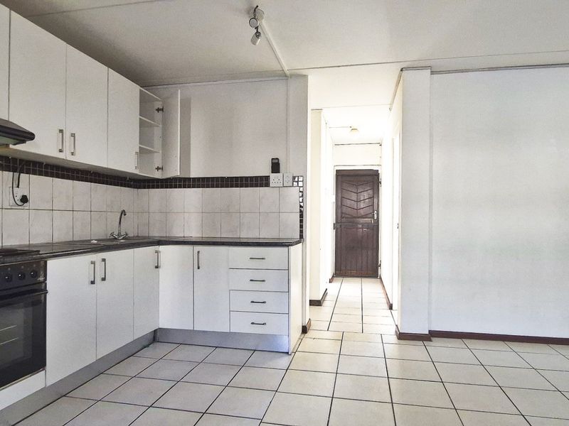Open plan kitchen area featuring white cabinetry, tiled flooring, and built-in appliances, leading to a hallway with a security gate.