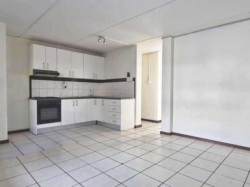 An open-plan kitchen and living area featuring tiled flooring, white built-in cabinetry, and an integrated oven with an extractor fan.