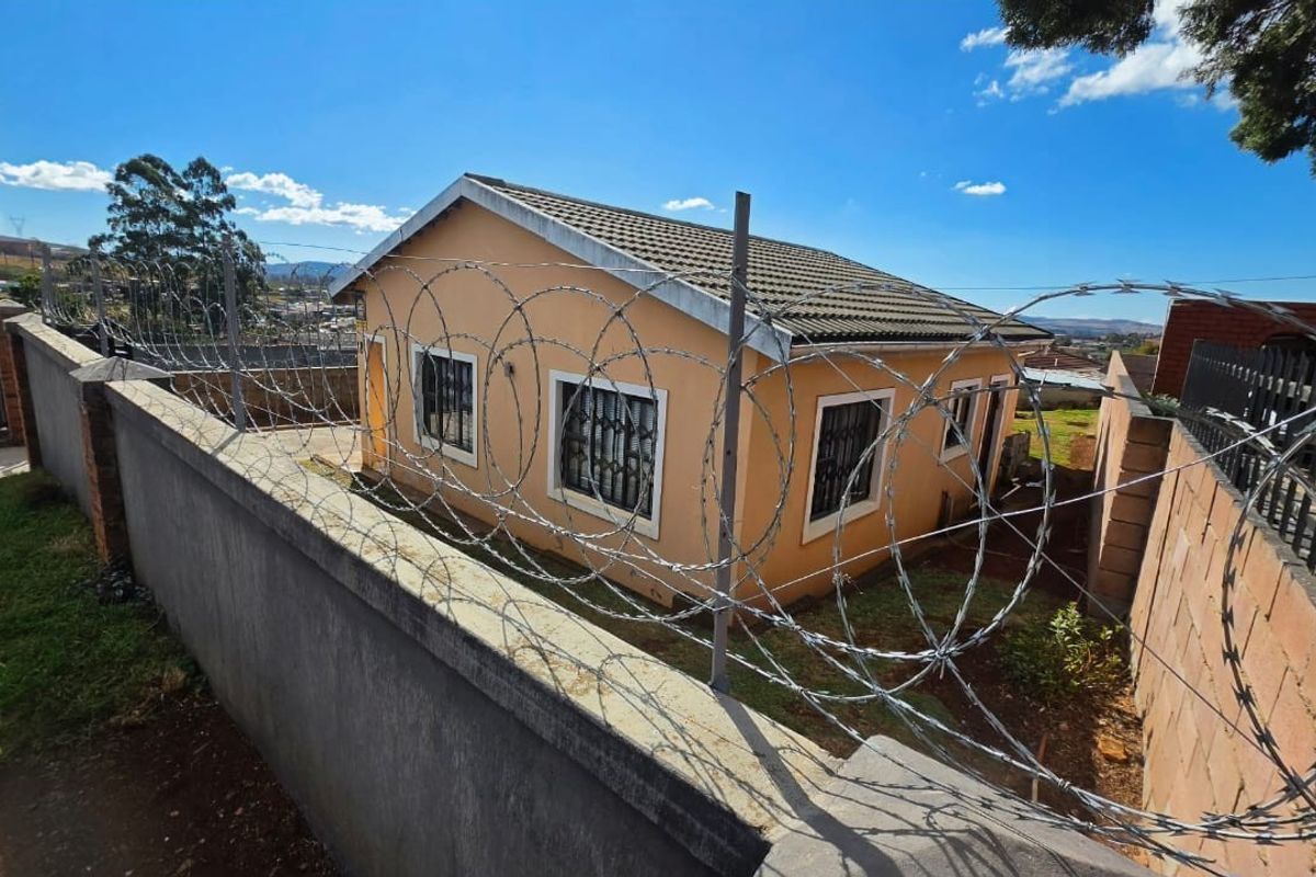 Rear view of a detached house featuring a concrete perimeter wall with security razor wire and tiled roof.