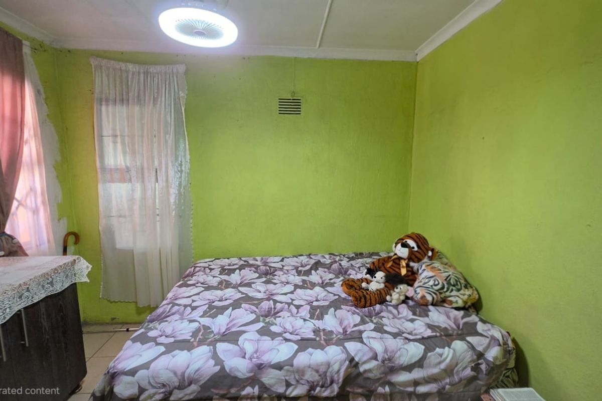 A bedroom featuring lime green walls, a ceiling fan, and a ventilation grille, requiring cosmetic updates to improve the overall finish.