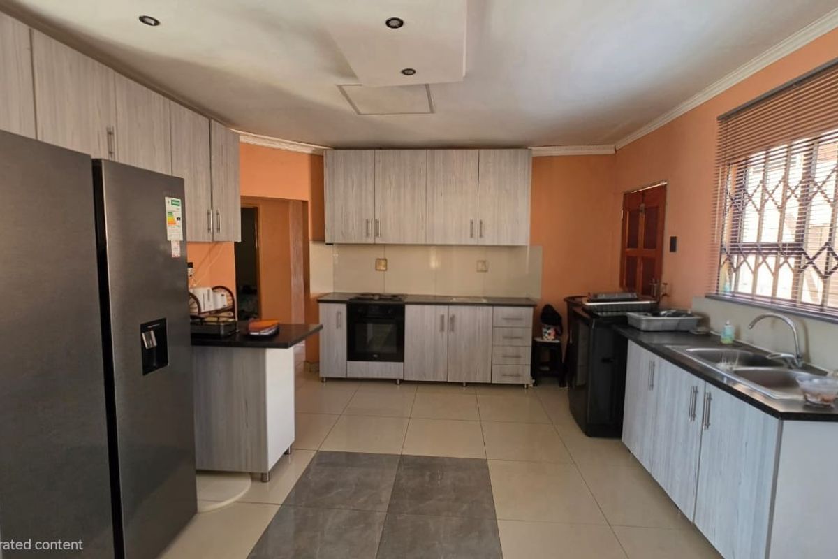 A functional kitchen featuring light wood-grain cabinetry, built-in oven and hob, double sink, and tiled flooring with security bars on the window.