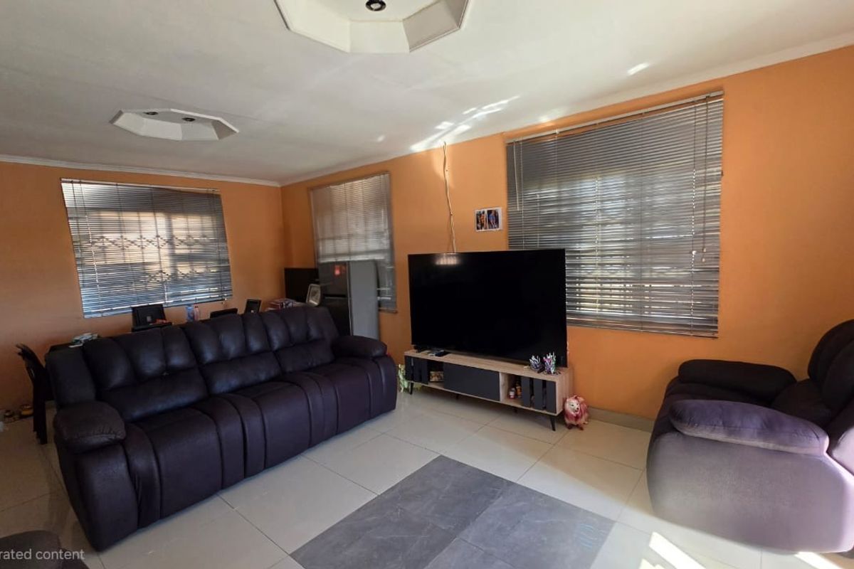 A spacious living room featuring tiled flooring, recessed ceiling details, and multiple windows fitted with venetian blinds, offering a bright and functional living space.