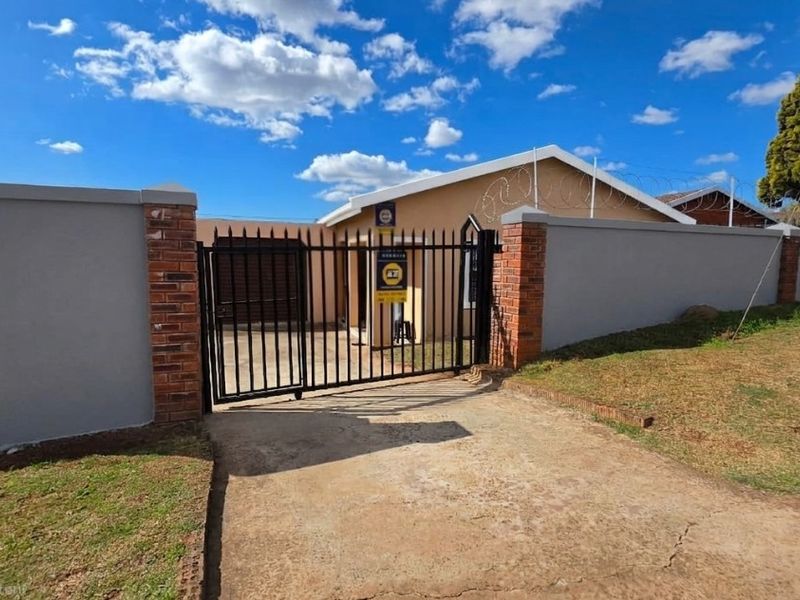 Front exterior view of the property featuring a secure perimeter wall, brick pillars, metal driveway gate, and concrete driveway.
