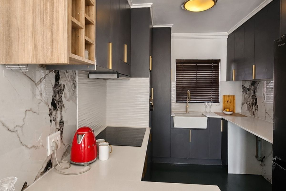 Modern galley kitchen featuring dark cabinetry, marble-look splashbacks, quartz countertops, an apron-front sink, and integrated induction hob with extractor fan.
