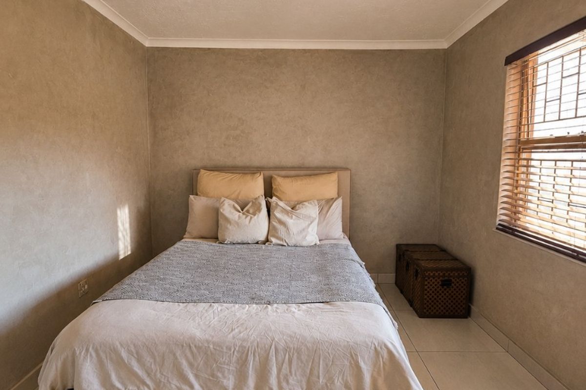 A well-maintained bedroom featuring neutral wall finishes, large format floor tiles, and venetian blinds providing natural light control.