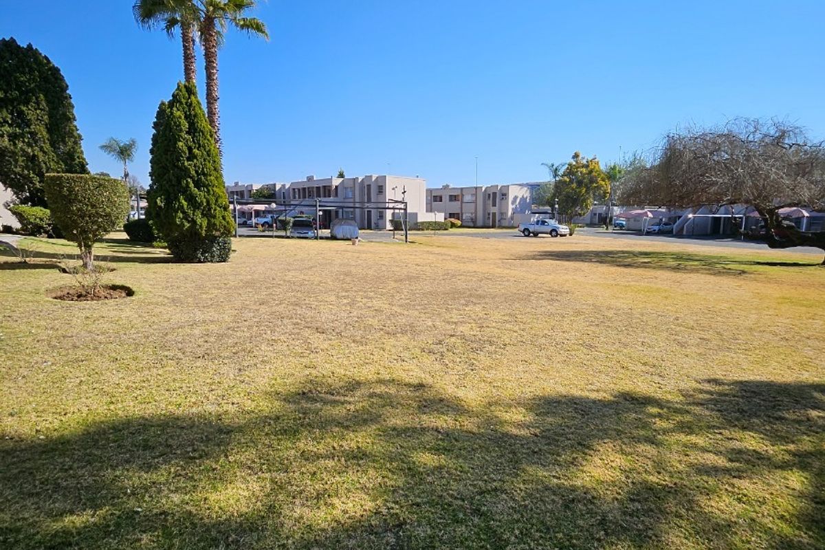 A wide-angle view of the communal garden area within the apartment complex, featuring established trees and open lawn space.