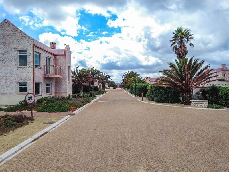 A view of a well-maintained residential street featuring paved roads, landscaped gardens, and brick-built residential properties under a cloudy sky.