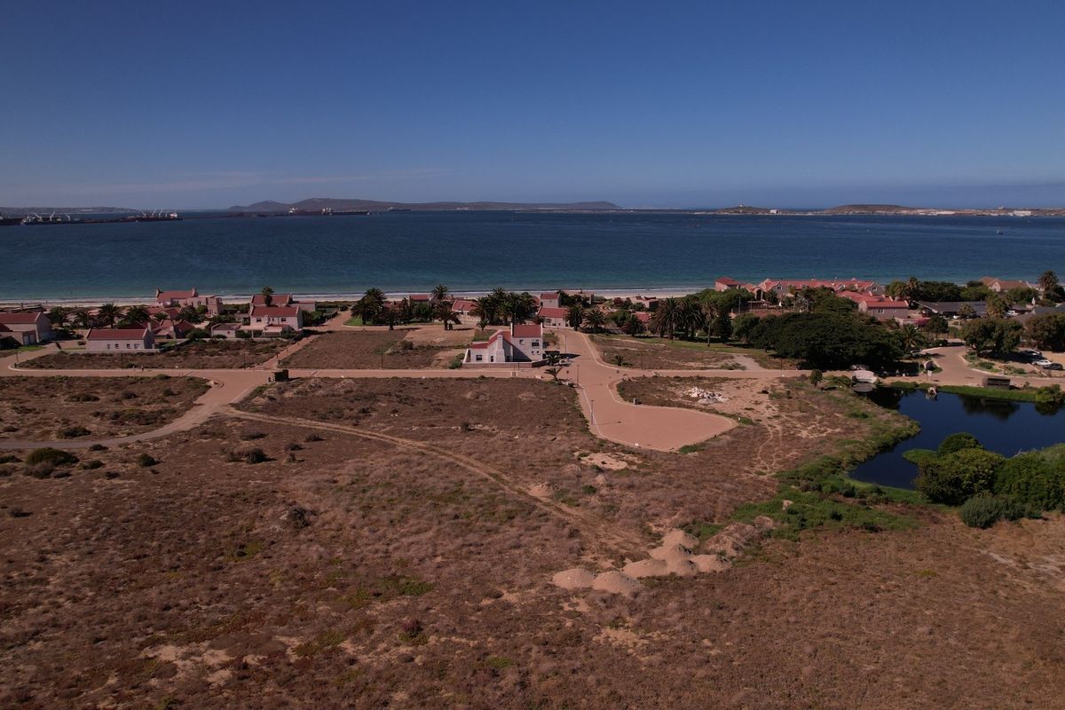Aerial view of a coastal residential development site featuring paved roads, natural vegetation, and proximity to the ocean.